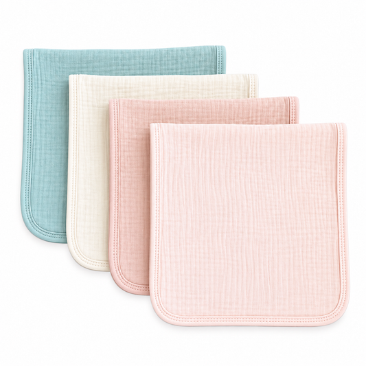 Four muslin baby burp cloths in pastel shades of light green, cream, dusty pink, and light pink arranged in a staggered stack on a white background.